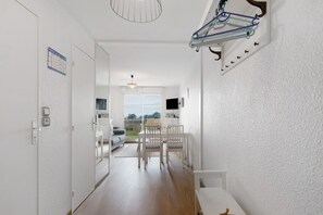 Un couloir avec une porte blanche, un calendrier, un porte-manteau et un coin repas avec des chaises et une table.