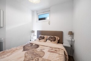 Un dormitorio con una cama, dos lámparas de noche, una ventana y un estante en la pared.