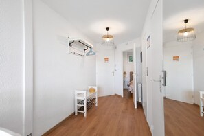 Ein Korridor mit weißen Wänden, Holzboden, einem Kleiderständer, einem kleinen Tisch mit einem Korb und einer Tür zu einem anderen Raum.