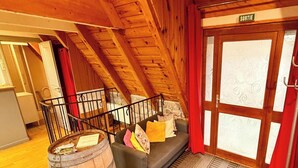 Um quarto acolhedor com teto de madeira, um sofá com almofadas, um barril de madeira e uma porta com a inscrição 'SORTIE'.