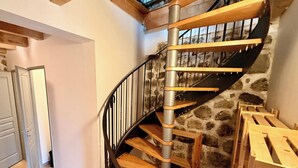 Uma escadaria em espiral com parede de pedra e degraus de madeira, que dá acesso a um andar superior.