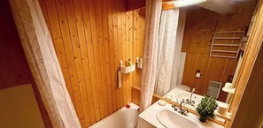 Ein Badezimmer mit Holzwandverkleidung, einer Badewanne, einem Waschbecken und einem Spiegel.