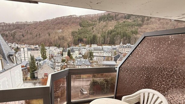 Ein Balkon mit Blick auf eine Stadt und bewaldete Hügel.