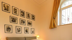Un lit bien fait, avec du linge de lit blanc et des serviettes pliées, un mur orné de tableaux encadrés, une fenêtre avec des rideaux et une lampe sur la table de chevet.