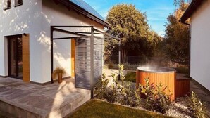 Ein modernes Haus mit Terrasse, Whirlpool und Garten mit verschiedenen Pflanzen.