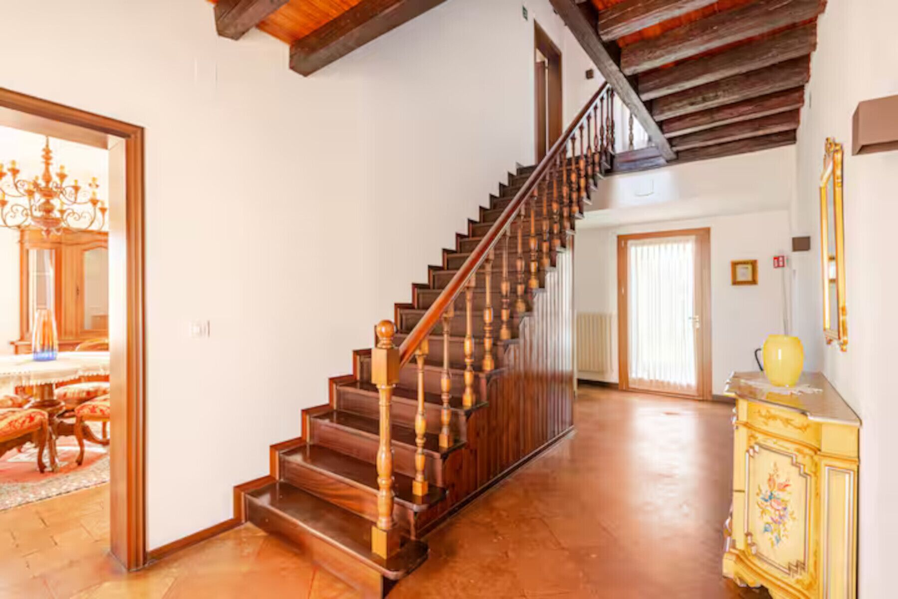 A spacious hallway with a wooden staircase, a chandelier, and a yellow cabinet.