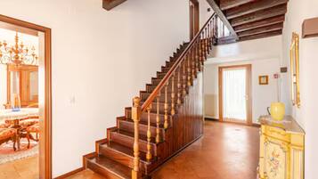 A spacious hallway with a wooden staircase, a chandelier, and a yellow cabinet.