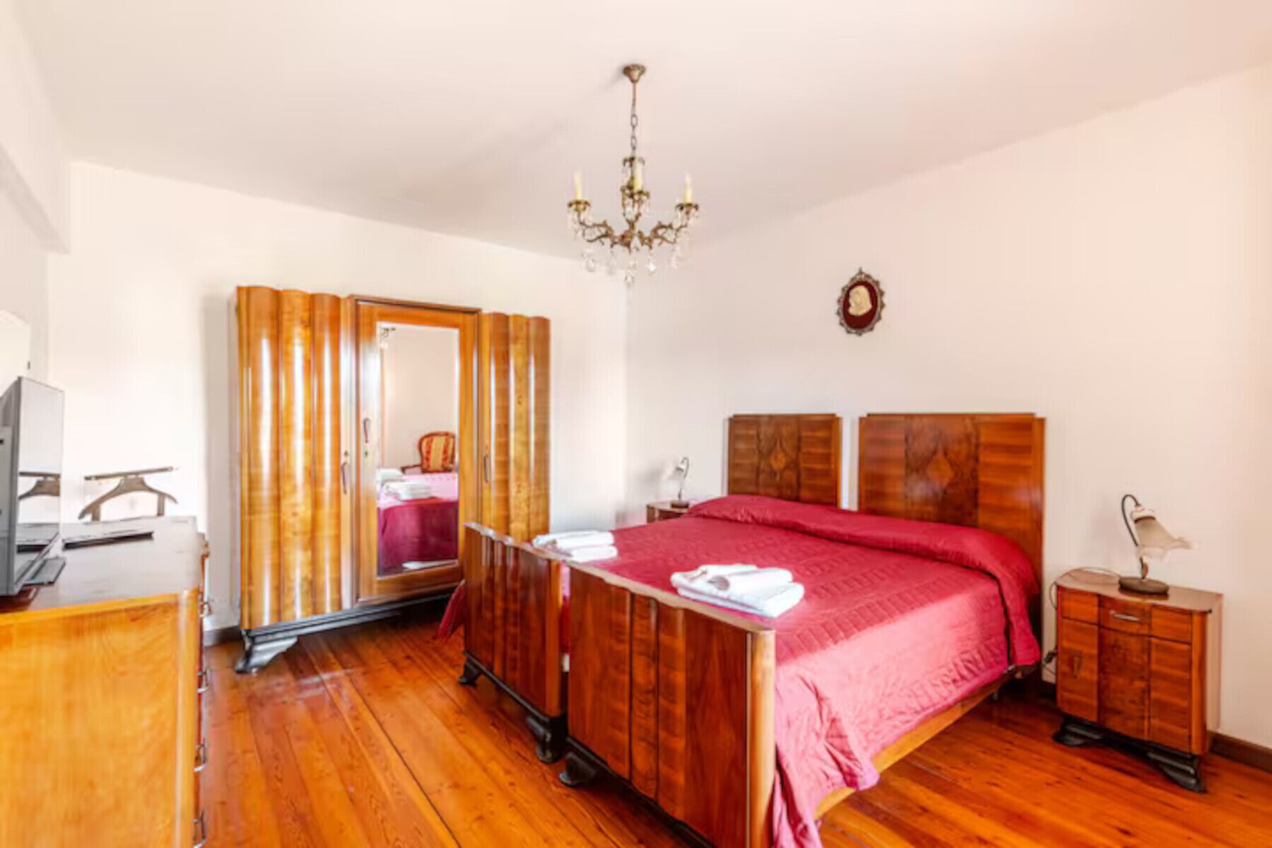 Ein Schlafzimmer mit einem hölzernen Bett, einem Schminktisch, einem Schreibtisch, einem Stuhl, einem Spiegel und einer Kronleuchter.