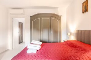 A hotel room with a bed, a wardrobe, a nightstand, and a painting on the wall.