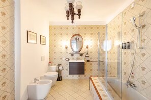 A bathroom with a toilet, bidet, sink, and bathtub. There is a mirror above the sink and a chandelier on the ceiling.