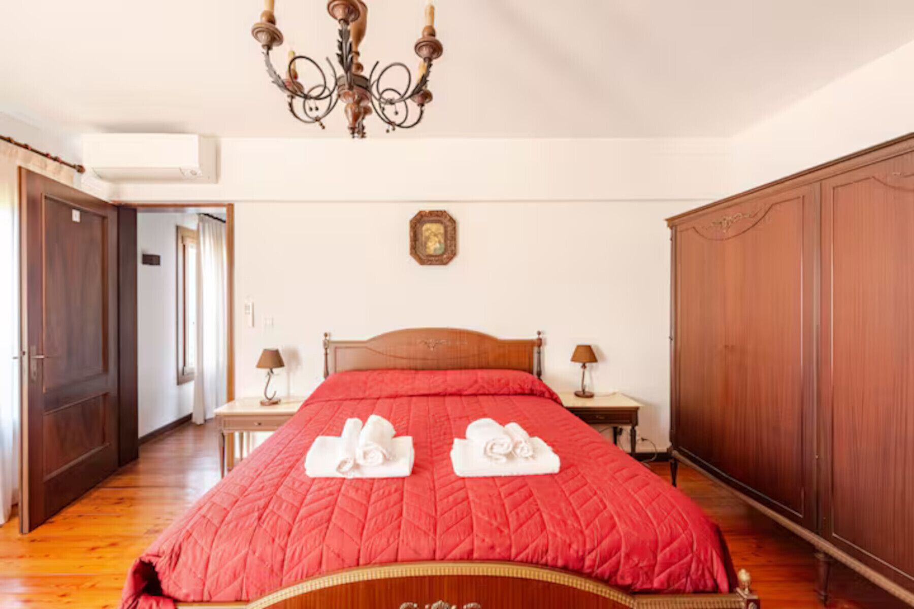 A bedroom with a wooden bed, two bedside tables, a chandelier, and a wardrobe.