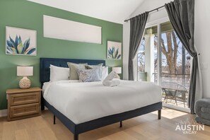Ein Schlafzimmer mit einem Bett, Nachttischen, einem Fenster mit Vorhängen und Kunstwerken an den Wänden.
