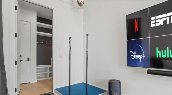 Una habitación con un colchoneta azul de ejercicios, un televisor con acceso a ESPN, Hulu y Disney+, y un altavoz JBL.