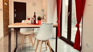 A dining area with a wooden table, two white chairs, a potted plant, and a bottle of wine. - Holiday home with jacuzzi, for 4 people (Rozewie)