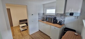 A compact kitchen with a microwave, toaster, and kettle on the countertop, a small window above the sink, and a white refrigerator with a Wi-Fi symbol. - Immensee Appartments by Mainka Properties (Immensee)