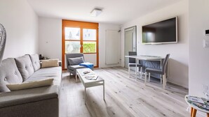 Una sala de estar moderna con un sofá, una mesa de centro, una zona de comedor con una mesa y sillas, y un televisor montado en la pared.