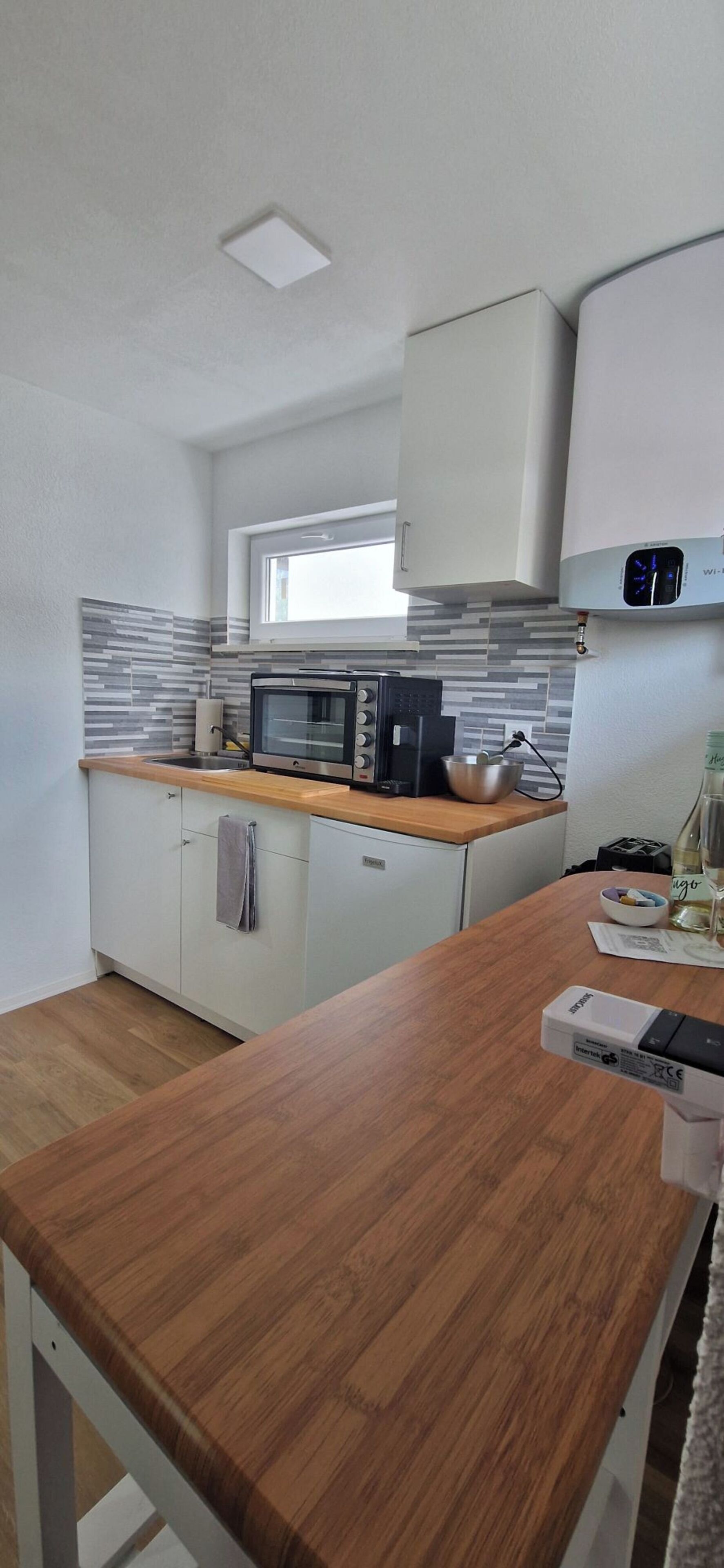 Una cocina moderna con armarios blancos, encimera de madera, microondas empotrado y una ventana sobre el fregadero.