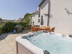 Ein Whirlpool im Garten mit Tisch und Stühlen, einem Grill und einer an der Wand befestigten Außenleuchte.