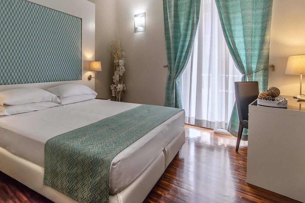 A neatly arranged hotel room with a bed, bedside lamps, a desk, and a window with curtains.