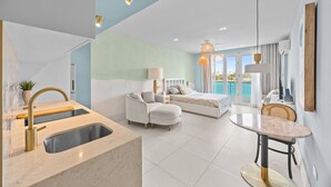 A modern hotel room with a kitchen area, a bed, a seating area, and a balcony with a view of the sea. - Perfect Couples Getaway with Ocean View Location (San Juan)