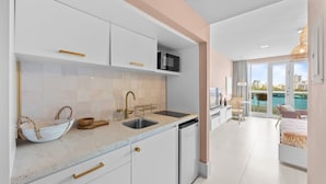 A modern kitchen with white cabinets, a microwave, and a sink. There is a dining area with a table and chairs, and a balcony with a view of the city. - Stylish 1BR with Balcony & Prime Location (San Juan)