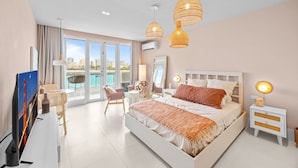 A modern hotel room with a large bed, a TV, a balcony with a view of the city, and a dining area with wicker furniture. - Stylish 1BR with Balcony & Prime Location (San Juan)