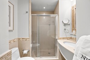 A bathroom with a glass-enclosed shower, a toilet, and a sink with a mirror. - Bright & Modern Suite for Couples (San Juan)
