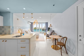 A modern kitchen with a central island, a dining area with a round table and chairs, and a view of a pool through the glass doors. - Bright & Modern Suite for Couples (San Juan)