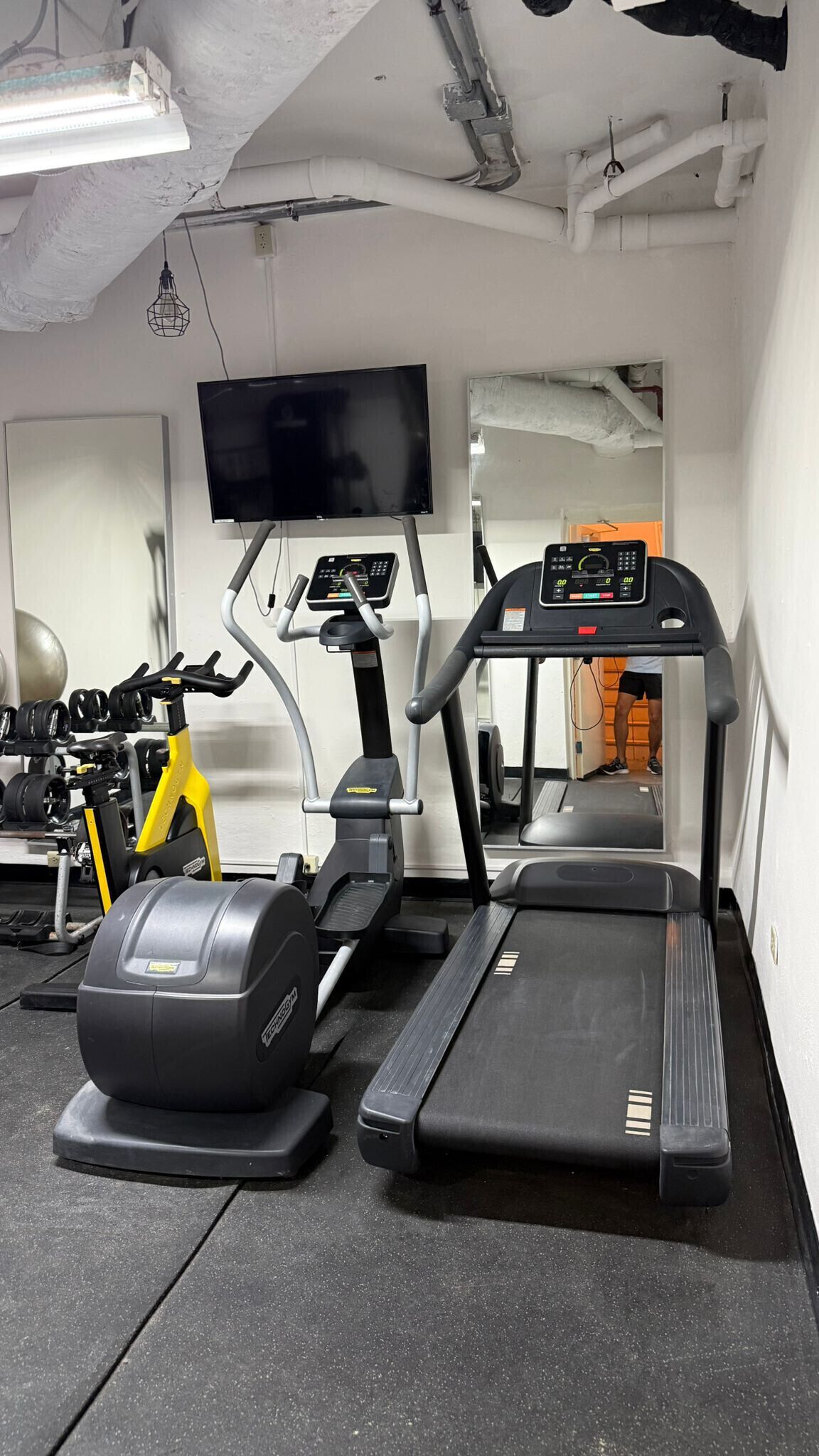 A gym with a treadmill, elliptical, and weight machine.