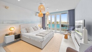 A modern bedroom with a large bed, bedside tables, a TV, and a view of a pool and cityscape. - Bright & Modern Suite for Couples (San Juan)