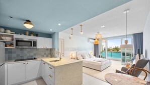 A modern kitchen with a central island, a dining area with a marble table, a bedroom with a large bed, and a balcony with a view of the sea. - Bright & Modern Suite for Couples (San Juan)