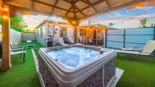 A hot tub under a covered patio with string lights, outdoor furniture, and a view of a house. - Tucson Norris House (Tucson)