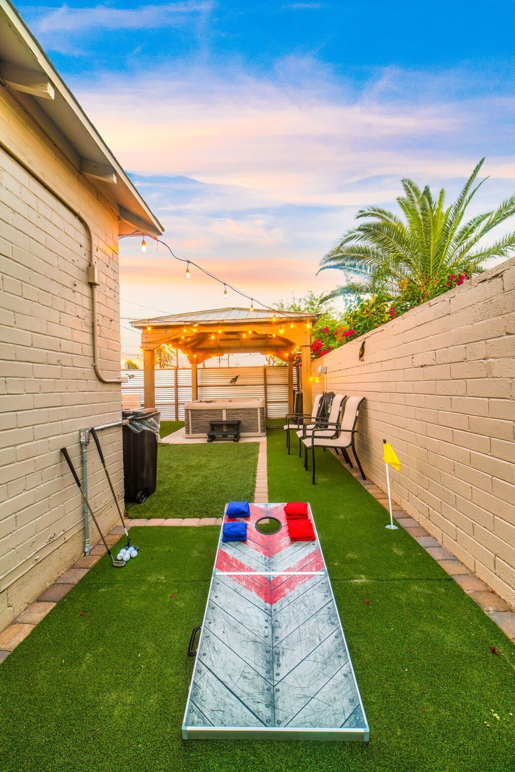 Ein Garten mit Kunstgrashalm, einem Shuffleboard-Tisch, Gartenmöbeln und einer Pergola mit Lichterketten.