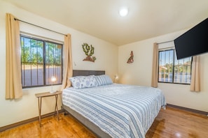 A bedroom with a bed, a nightstand, a lamp, a window with curtains, and wall art. - Tucson Norris House (Tucson)