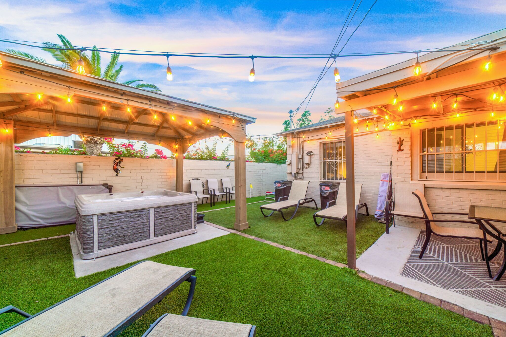 A backyard patio with a hot tub, outdoor seating, and string lights.