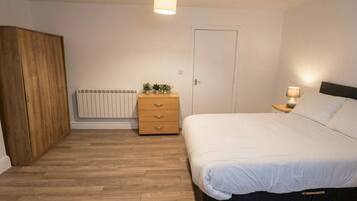 Ein Schlafzimmer mit einem Bett, einem Holzschrank, einem Nachttisch mit Lampe, einem Heizkörper und einer Tür.