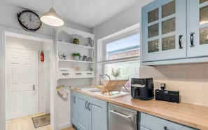 A modern kitchen with light blue cabinets, a wooden countertop, a coffee maker, and a clock on the wall. - Bay Tree Cottage (King's Lynn)