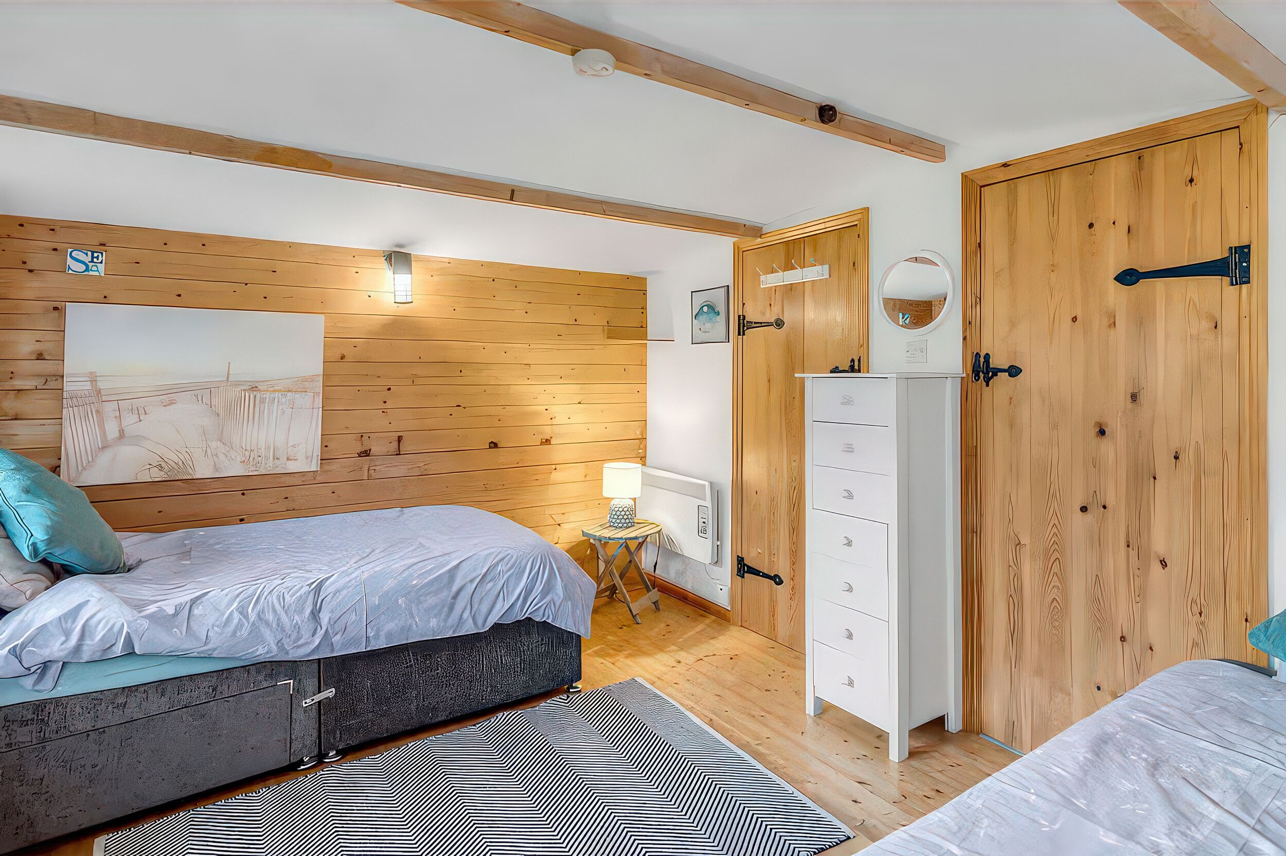 A bedroom with two beds, wooden walls, a dresser, a mirror, and a painting.