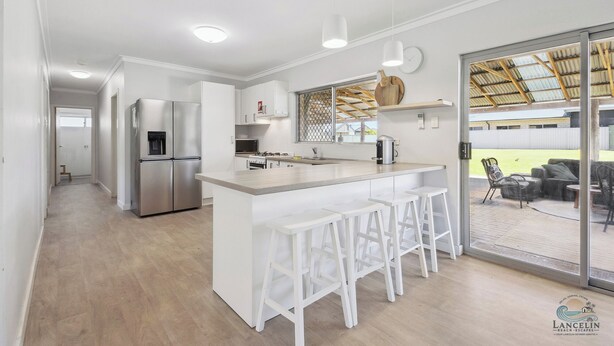 Eine moderne Küche mit weißen Schränken, Edelstahlgeräten und einer Bar mit weißen Hocker.