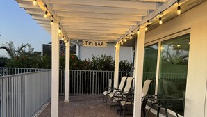 A covered patio area with a sign reading "TIKI BAR," featuring a brick floor, metal chairs, and string lights.