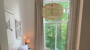 Un dormitorio con cama, ventana con cortinas, lámpara colgante y decoración en la pared.