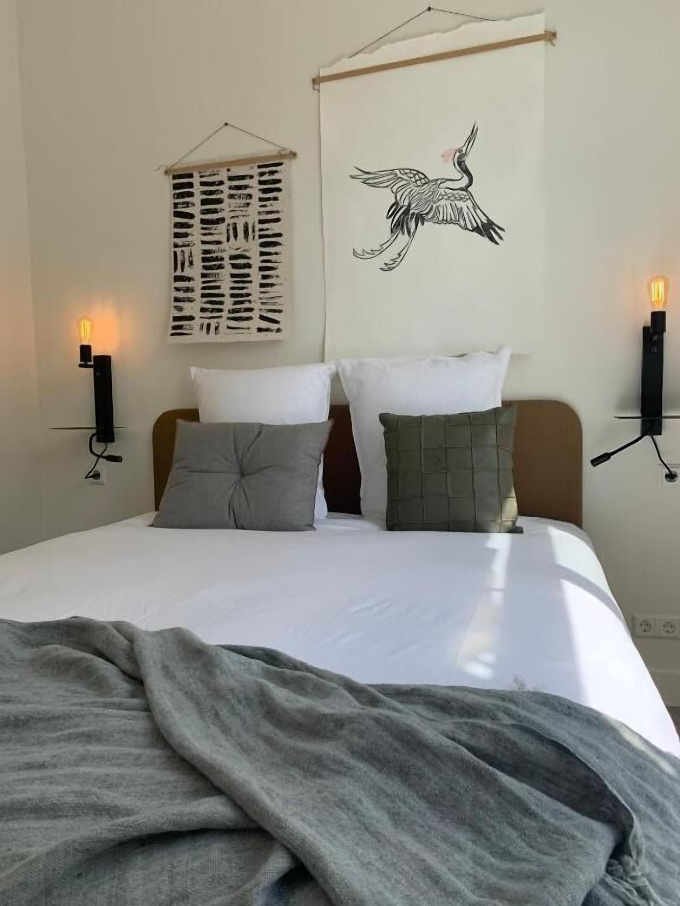 A neatly made bed with two pillows, a blanket, and a wall-mounted artwork of a bird.