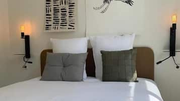 A neatly made bed with two pillows, a blanket, and a wall-mounted artwork of a bird.