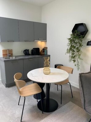 A modern kitchen with grey cabinets, a round marble table, and two wooden chairs.