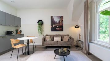A modern living room with a round table, two chairs, a sofa, and a large window.