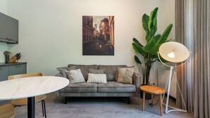 Una sala de estar moderna con un sofá gris, una mesa redonda, una lámpara de pie y una planta verde grande.