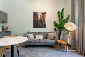 A modern living room with a grey sofa, a round table, a floor lamp, and a large green plant. - Utrecht City Apartments Maliesingel (Utrecht)