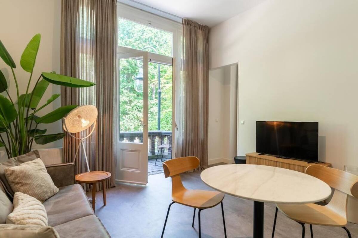 Una sala de estar moderna con un sofá, una mesa redonda, dos sillas, un televisor y una planta grande.