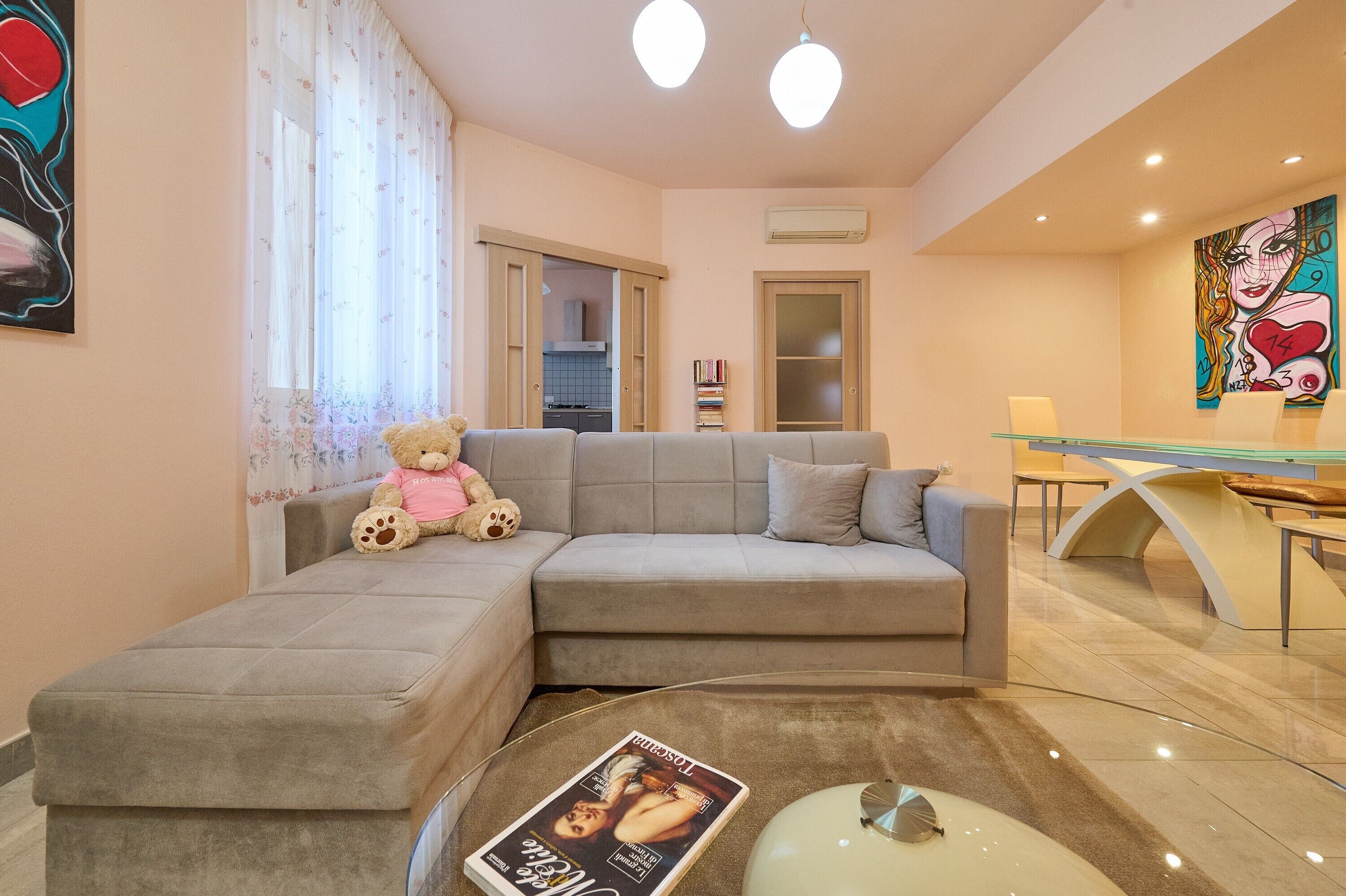 Uma sala de estar com um sofá, um urso de pelúcia, uma revista sobre uma mesa de centro e um quadro na parede.