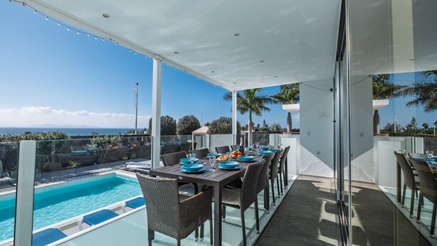 Terraza en la azotea con piscina, mesa de comedor dispuesta con platos y vasos, y una vista despejada del océano.